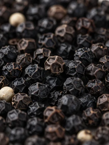 Schwarze Pfefferkörner und gemahlener Pfeffer in Keramikschale und auf Holzoberfläche