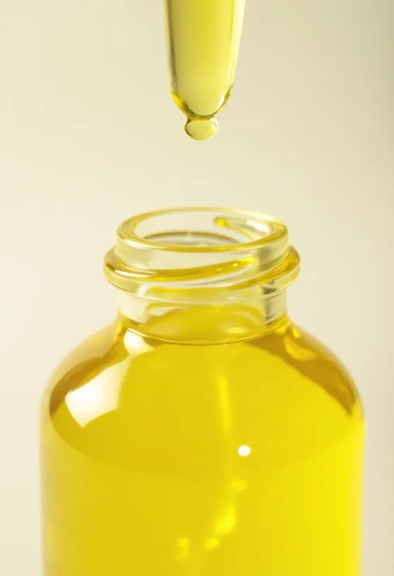 Zitronenöl in kleiner Flasche, neben frischen Zitronenscheiben und geriebener Schale