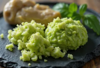 Frische Wasabiwurzel und grüne Wasabipaste auf Holzoberfläche, in Schale und auf Reibe
