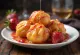 Loukoumades mit Erdbeermarmelade, goldbraune Bällchen mit roter Marmelade übergossen und Puderzucker bestäubt